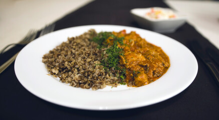 Serving of appetizing dish on table in restaurant. Buckwheat, goulash with dill in white plate.