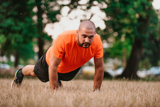 Young man working out doing push-ups in park as he warms up for his daily workout or jog