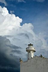 A lighthouse on an old building in Telchac Puerto on the coast of Yucatán on the Gulf of Mexico, cormorants sitting on the roof, big storm clouds in the background