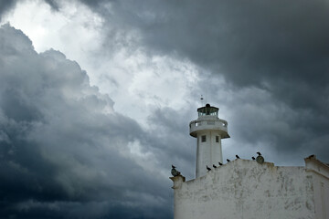 A lighthouse on an old building in Telchac Puerto on the coast of Yucatán on the Gulf of Mexico, cormorants sitting on the roof, big storm clouds in the background - obrazy, fototapety, plakaty