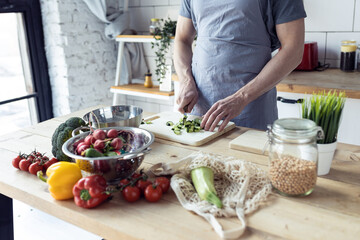 Handsome father, strong young man cooking healthy vegetable salad with fresh organic ingredients, tasty food in the kitchen at home . Men doing chores. Ripe pepper, tomato, cucumber