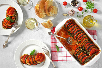 Delicious ratatouille in baking dish and plates on white table, and glasses of wine. dinner concept