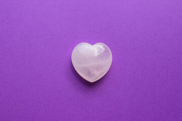 A beautiful heart-shaped rose quartz crystal lies on a lilac background. Rose quartz is a stone for success in love for women.