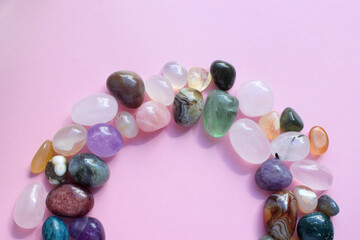 The circle is lined with natural minerals. Semi-precious stones of different colors, raw and processed. Amethyst, rose quartz, agate, apatite, aventurine on a pink background.