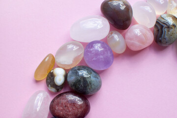 Semi-precious beautiful stones of bright colors lie on a pink background. Amethyst, rose quartz, agate, apatite, aventurine, rock crystal on a pink background. Selective focus.