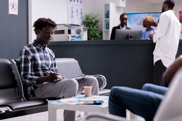 African american patient filling in report papers before checkup visit appointment with doctor. Writing medical form on files in waiting area lobby to attend consultation and examination with medic.