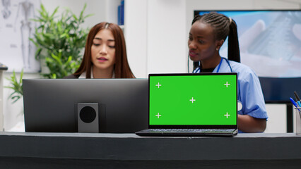 Diverse receptionist and nurse working with greenscreen on laptop at reception counter desk. Isolated mockup template with copyspace display and blank chroma key background at medical center.