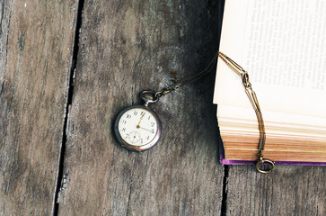Eine antike Taschenuhr und ein altes Buch auf einem alten Holztisch - obrazy, fototapety, plakaty