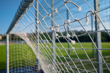 closeup of soccer gate goalpost white rope net with green field in background