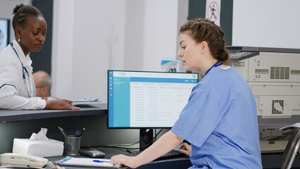 Medical assistant working on patient appointments at reception desk, helping african american doctor with information to do consultation with senior man. Diverse staff at healthcare clinic.