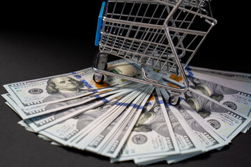 shopping cart trolley with money, pack of hundred dollar bills on black background, concept of buying, money spending, black Friday sale, currency