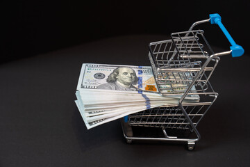 shopping cart trolley with money, pack of hundred dollar bills on black background, concept of...