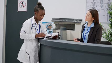 Portrait of african american doctor analyzing medical report papers with receptionist at hospital...
