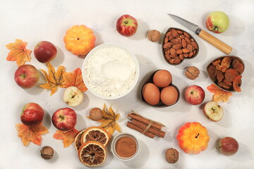 Kitchen background with pumpkin, apples, spices, nuts, flour, eggs and seasonal leaves, cooking concept, ingredients for pumpkin and apple pies recipe, selective focus, top view,