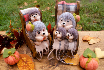 Felted grandfather and grandmother hedgehogs in armchairs with blankets near their grandchildren small hedgehogs made also of wool on a wooden background with autumn decor