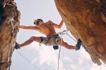 Fototapeta na wymiar Fitness, rock climbing and strong mountain climber on a cliff with ropes in summer challenge and extreme exercise. Danger, courage and healthy man fearless, sports and big rocks or stone below view