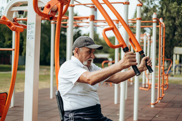Persistent mature man with disabilities doing fitness exercises on outdoor simulator, pumping...