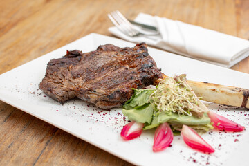 Different cuts of meat, chicken and pork on a white plate on a light wooden background
