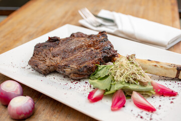 Different cuts of meat, chicken and pork on a white plate on a light wooden background
