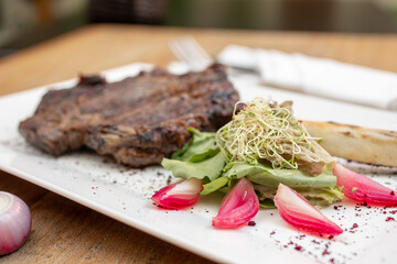 Different cuts of meat, chicken and pork on a white plate on a light wooden background
