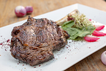Different cuts of meat, chicken and pork on a white plate on a light wooden background
