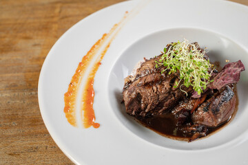 Different cuts of meat, chicken and pork on a white plate on a light wooden background
