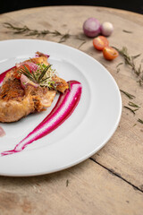 Different cuts of meat, chicken and pork on a white plate on a light wooden background
