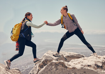 Happy women help while hiking up a rocky mountain in nature with backpack. Females friends exercise...