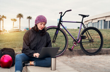 Fototapeta na wymiar young latin woman cyclist sitting outdoors on a step with a laptop working happy