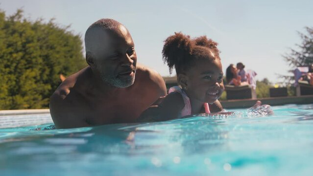 Grandfather teaching granddaughter to swim in outdoor pool on summer holiday - shot in slow motion