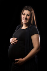 Young brunette woman at late stages of pregnancy smiles and poses with her baby bump, studio light used.