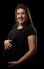 Young brunette woman at late stages of pregnancy smiles and poses with her baby bump, studio light used.