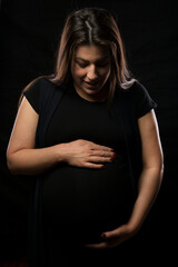 Young brunette woman holding her pregnant belly, studio light used.