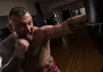 Topless tattoos man left jabs a punch bag with an aggressive face.
