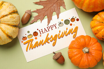 Pumpkins, acorns, autumn leaves and greeting card for Thanksgiving Day on green background