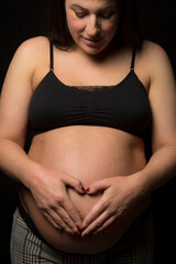 Young Brunette woman looking down at her big baby bump, studio light used.