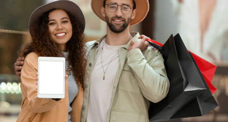 Couple with tablet computer and shopping bags on city street