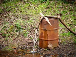 Water from the hose flows into the pond. Rusty barrel in nature by the pond.