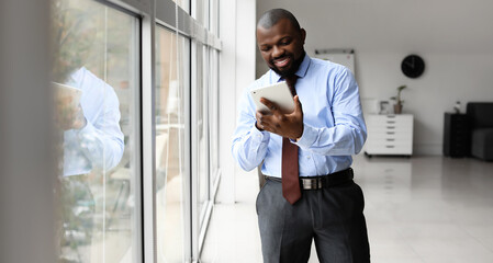 Handsome African-American businessman with tablet computer near window in office