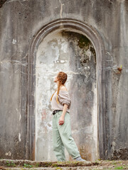 Obraz premium Woman in arch of ancient architecture outdoors. Arched stone stucco structure of ancient architecture. Tourist walk through abandoned places
