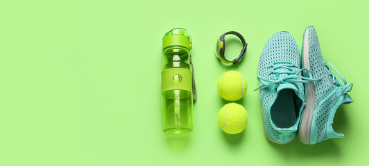 Sport shoes, bottle of water, fitness tracker and tennis balls on green background