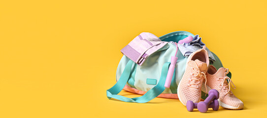 Bag with sportswear and equipment on yellow background