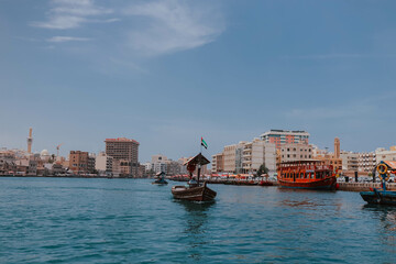 Obraz premium Dubai, UAE - April 15, 2021: Cityscape view of Dubai Creek channel with old wooden traditional boats cruising and piers. Sunny summer day. Famous tourist destination in UAE, United Arab Emirates. Abra
