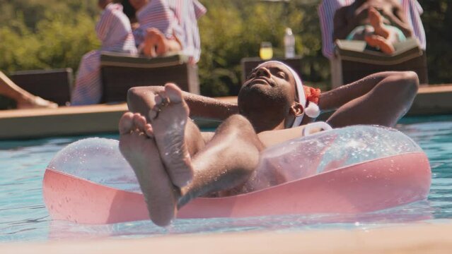 Man on family Christmas holiday floating in inflatable ring in swimming pool wearing santa hat - shot in slow motion
