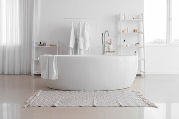 Naklejka na ściany i meble Interior of stylish bathroom with modern bathtub and shelf units with accessories near white wall