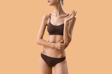 Slim young woman in underwear on beige background