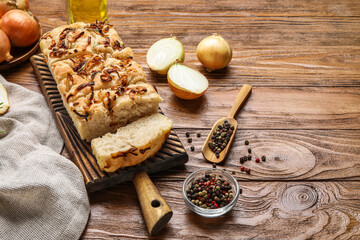 Board with tasty Italian focaccia, onion and peppercorns on wooden background