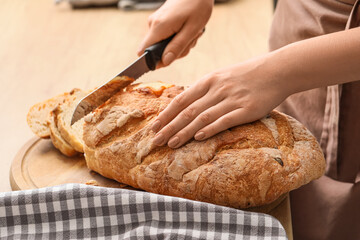 Woman cutting fresh bread on table in kitchen, closeup