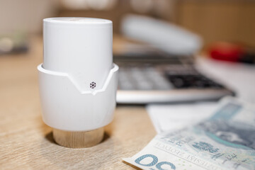 Thermostatic head for the radiator, in the background a calculator, money and documents (selective focus, blur)
