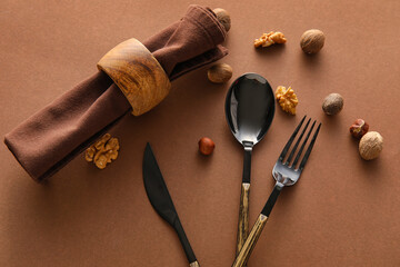 Napkin, cutlery and scattered nuts on brown background